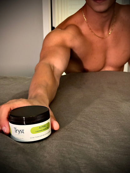 Person holding a jar of 'Tryst' scrub on a bed