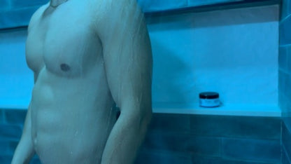 Man standing in a tiled shower room with a blue hue, with a Tryst container on the ledge